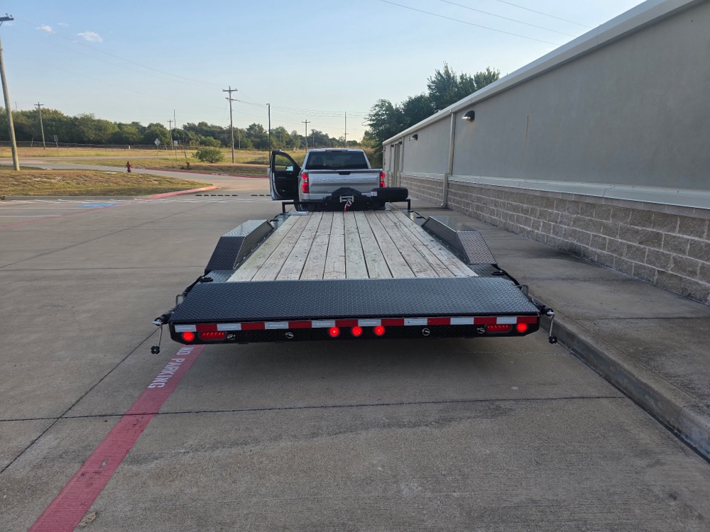 Rear view of the super-wide car hauler hitched to a pickup, showing the wide wood deck, loading area, and tail lights